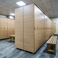 Wooden lockers with a wood bench in a locker room with doors closed. Locker room interior in modern fitness gym